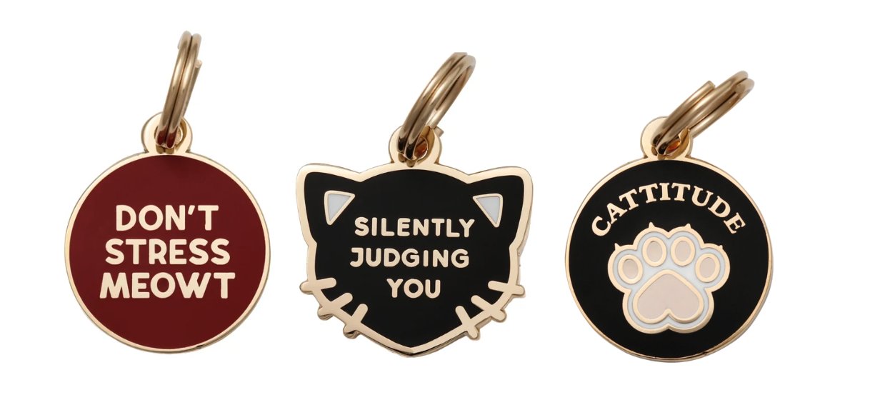 Three enamel and gold collar tags reading Don't Stress Meowt, Silently Judging You, and Cattitude