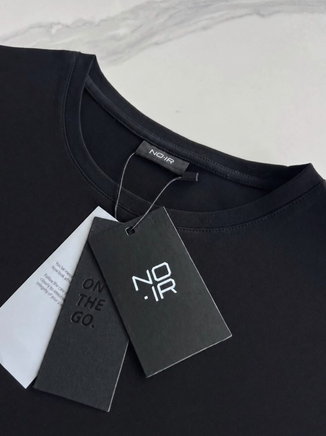 Embossed NOIR hang tags and care card on a tee, reading On the go