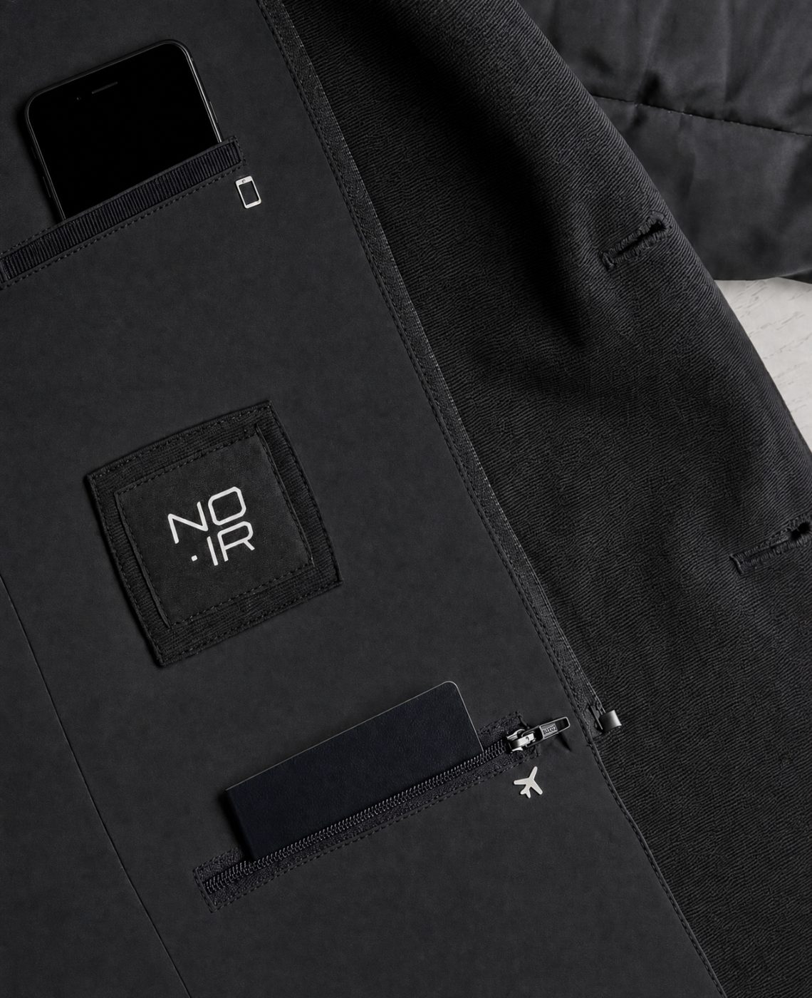 Interior pocket system laid flat, phone pocket marked with its own icon beside the NOIR patch