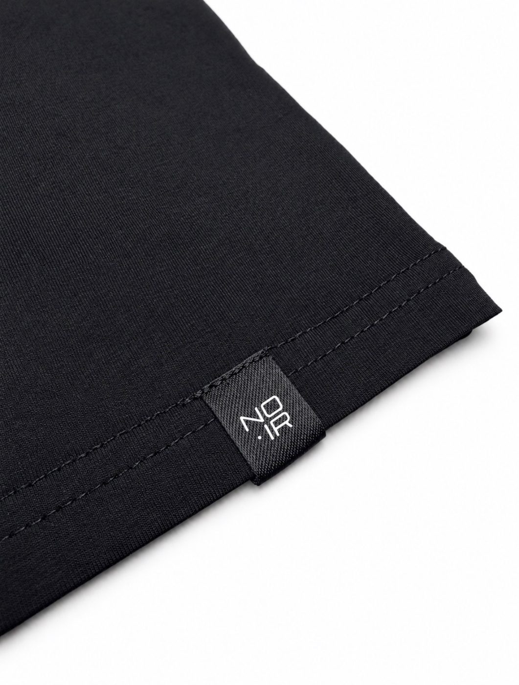 Woven NOIR tab label stitched into the hem of a tee
