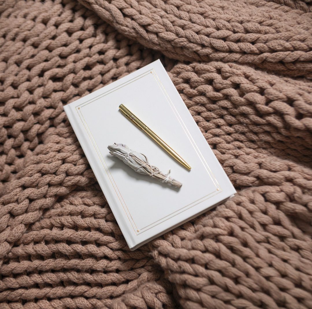 The foil edged journal with gold pen and sage on a knit throw