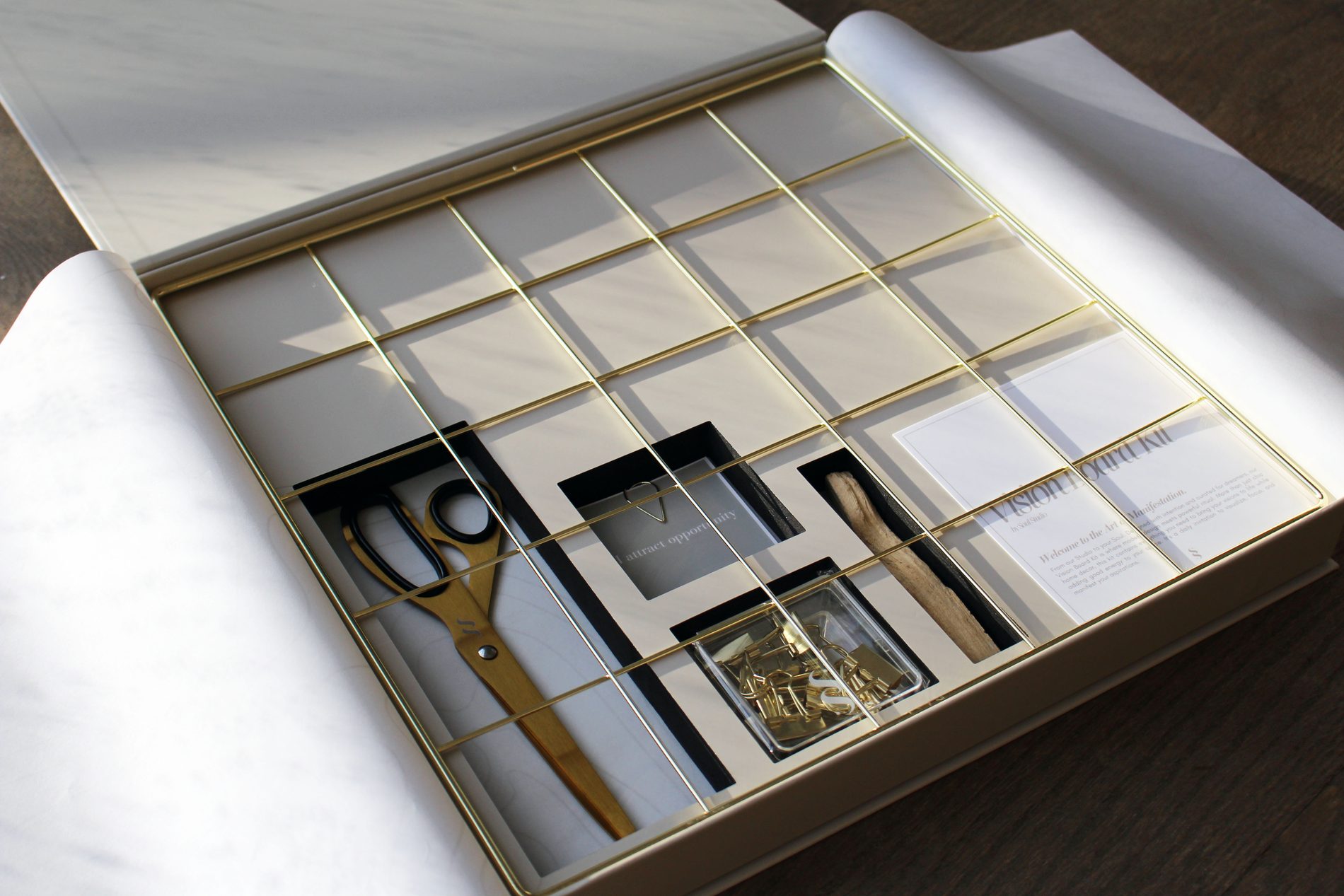 The Vision Board Kit opened, gold grid over compartments holding shears, clips, palo santo and printed cards